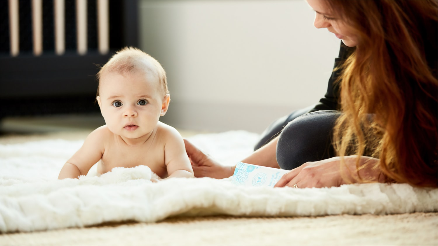Baby liegt auf dem Bauch auf einem Fell, die Mutter daneben