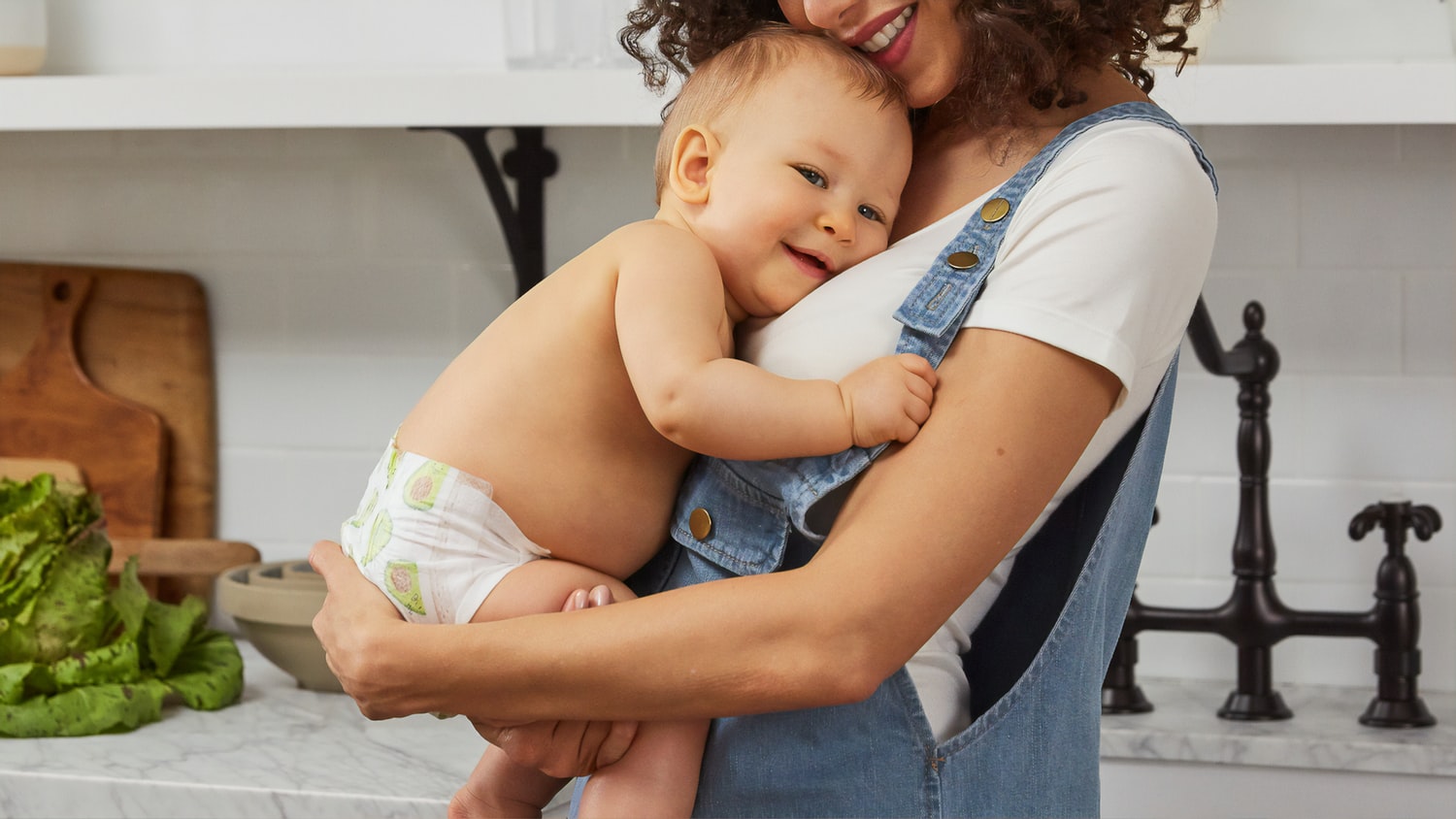 Mutter hält ihr Baby auf dem Arm, im Hintergrund die Küchenzeile