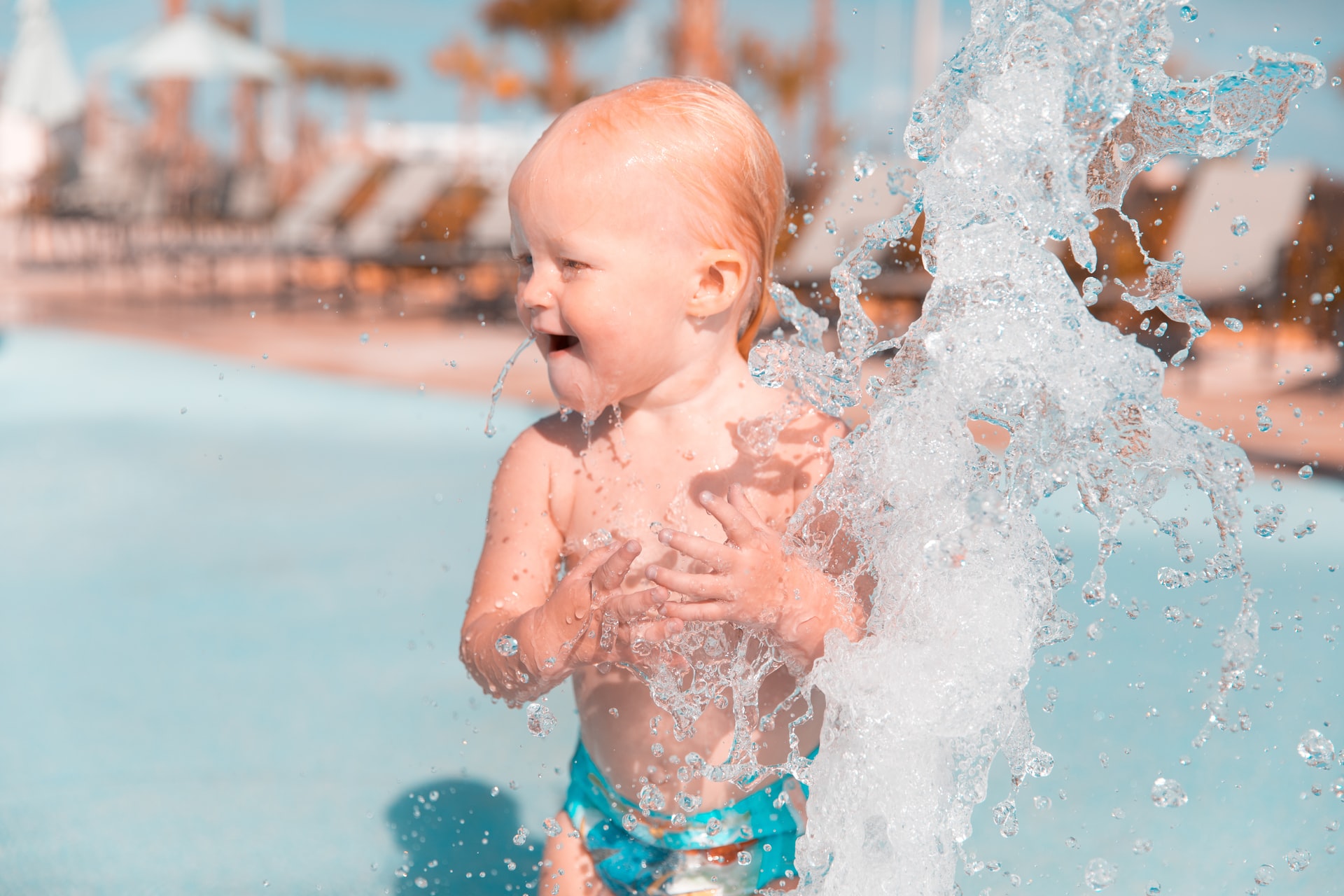 Kleinkind planscht lachend im Wasser eines Pools