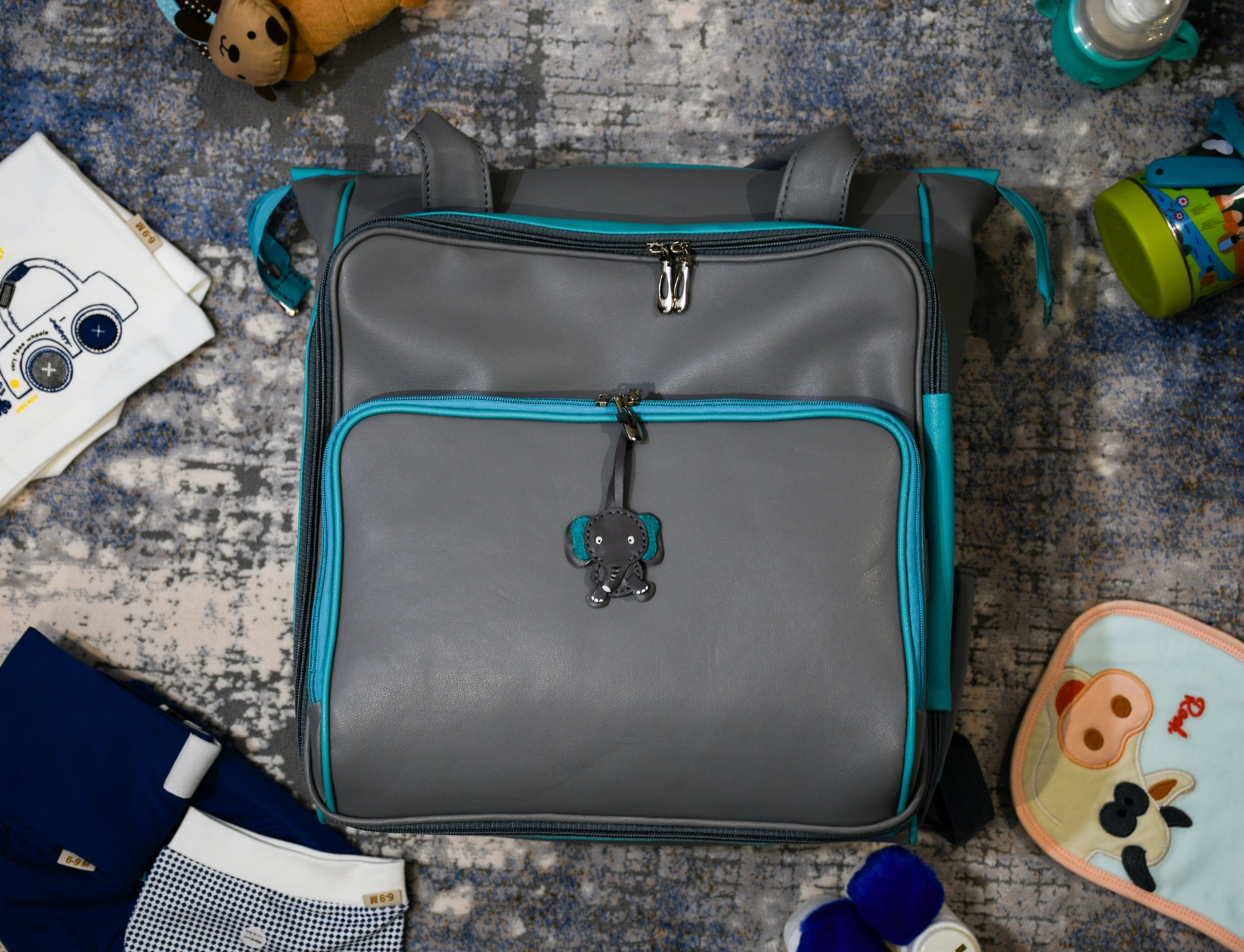 Gepackte Kliniktasche, darum herum Babykleidung, Fläschchen und Spielzeug