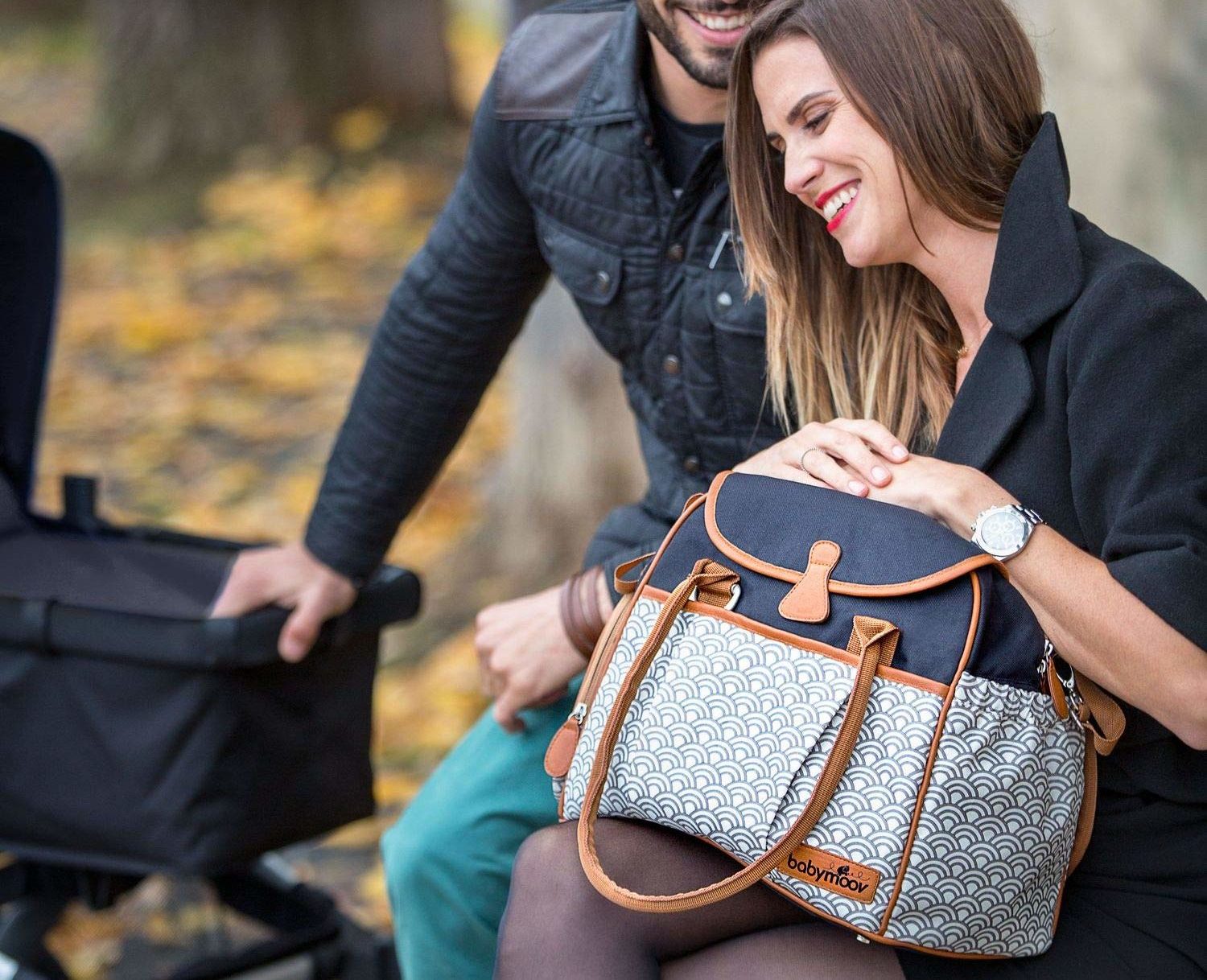 Mutter mit einer Wickeltasche auf dem Schoß sitzt mit dem Vater im herbstlichen Park