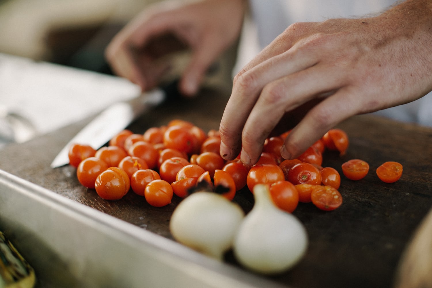 Hände schneiden Tomaten und Zwiebeln auf einem Holzbrett