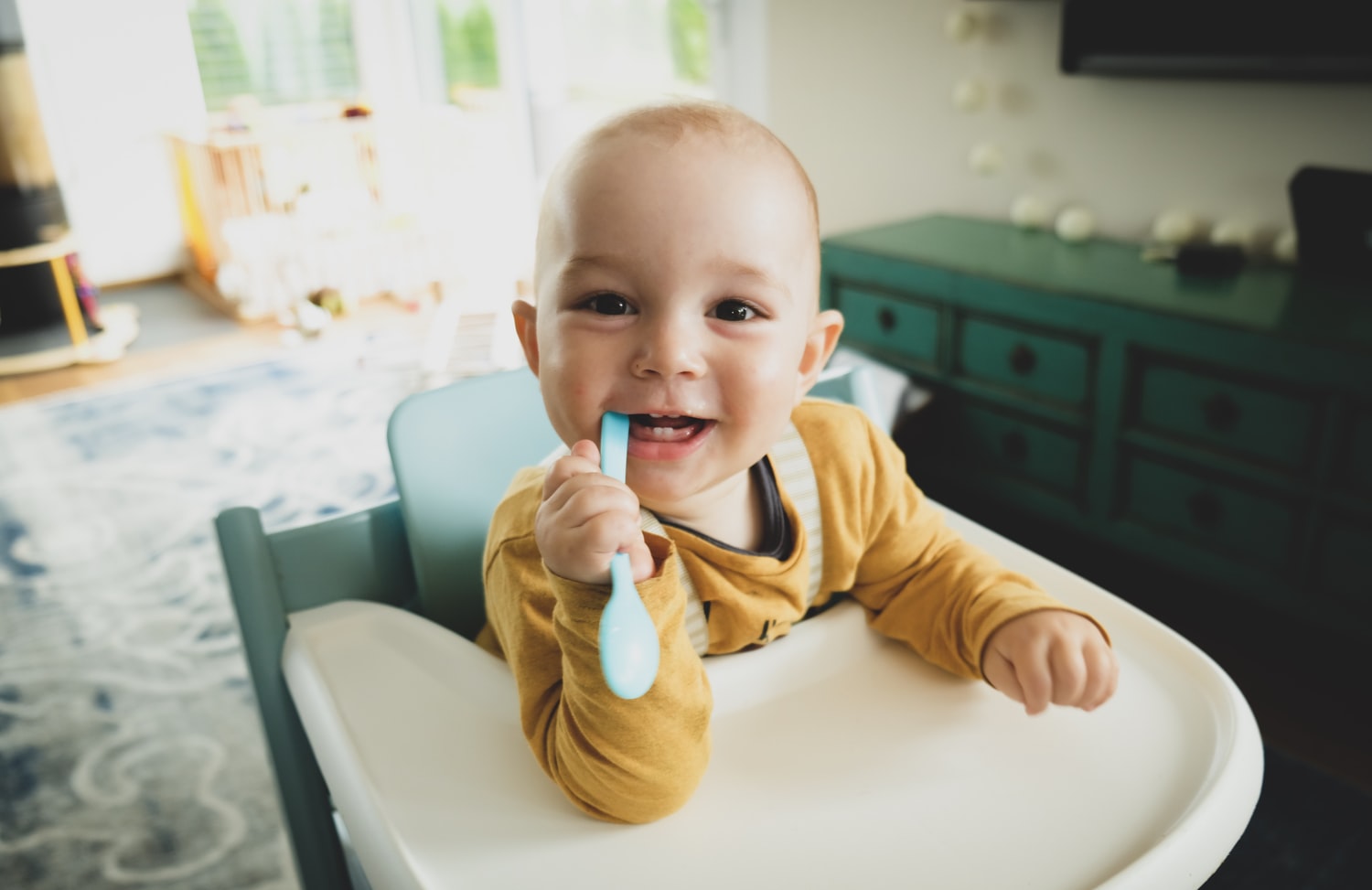 Baby sitzt im Hochstuhl und hält einen Löffel im Mund