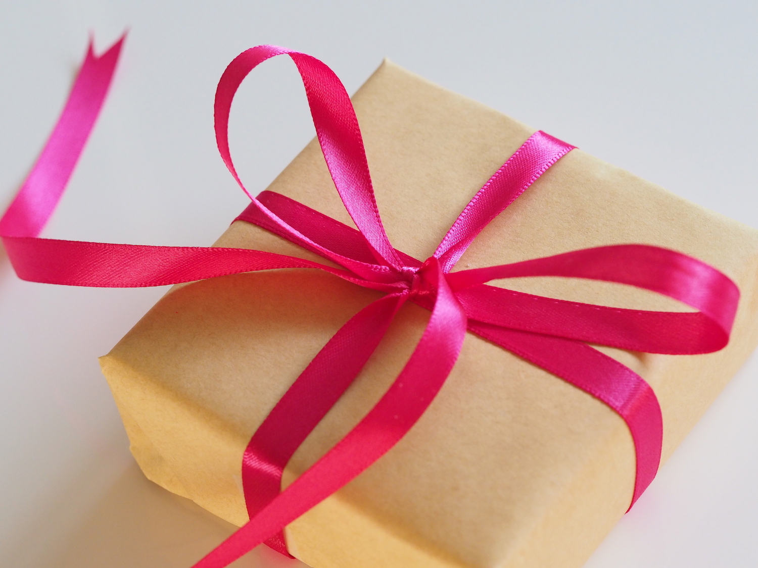 In Packpapier eingeschlagenes Geschenk mit pinkfarbener Schleife