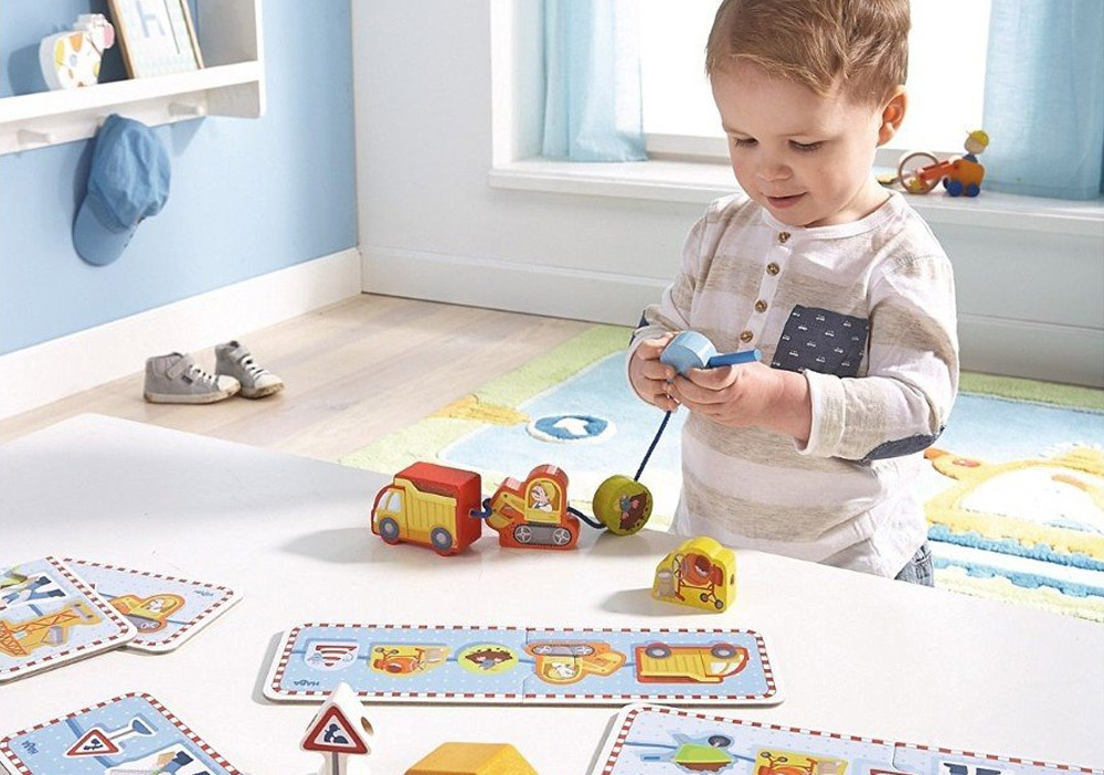 Kleinkind steht im Kinderzimmer zwischen Legekarten und Holzspielzeug