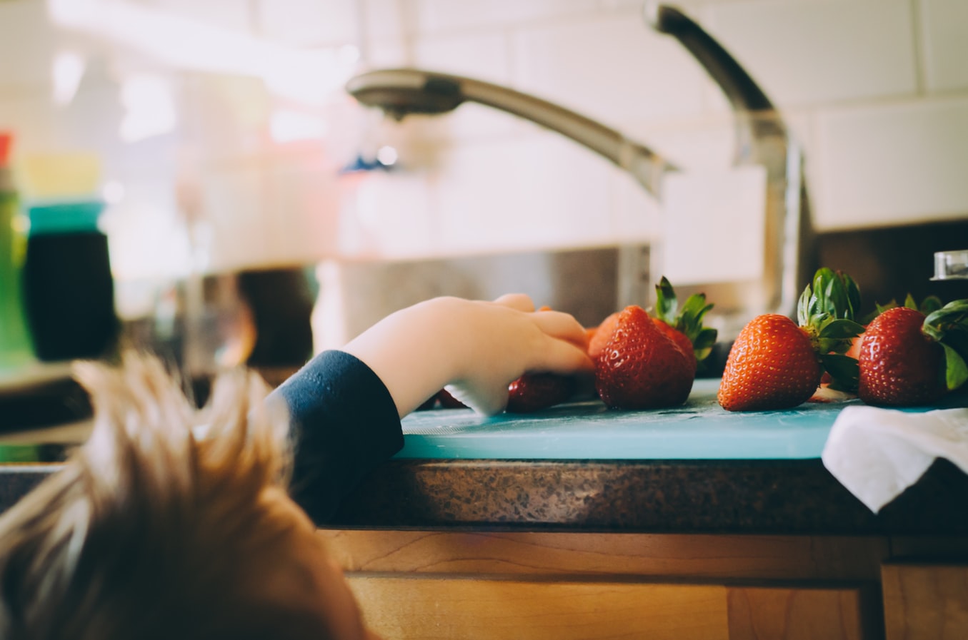 Kind greift auf der Küchenzeile nach Erdbeeren