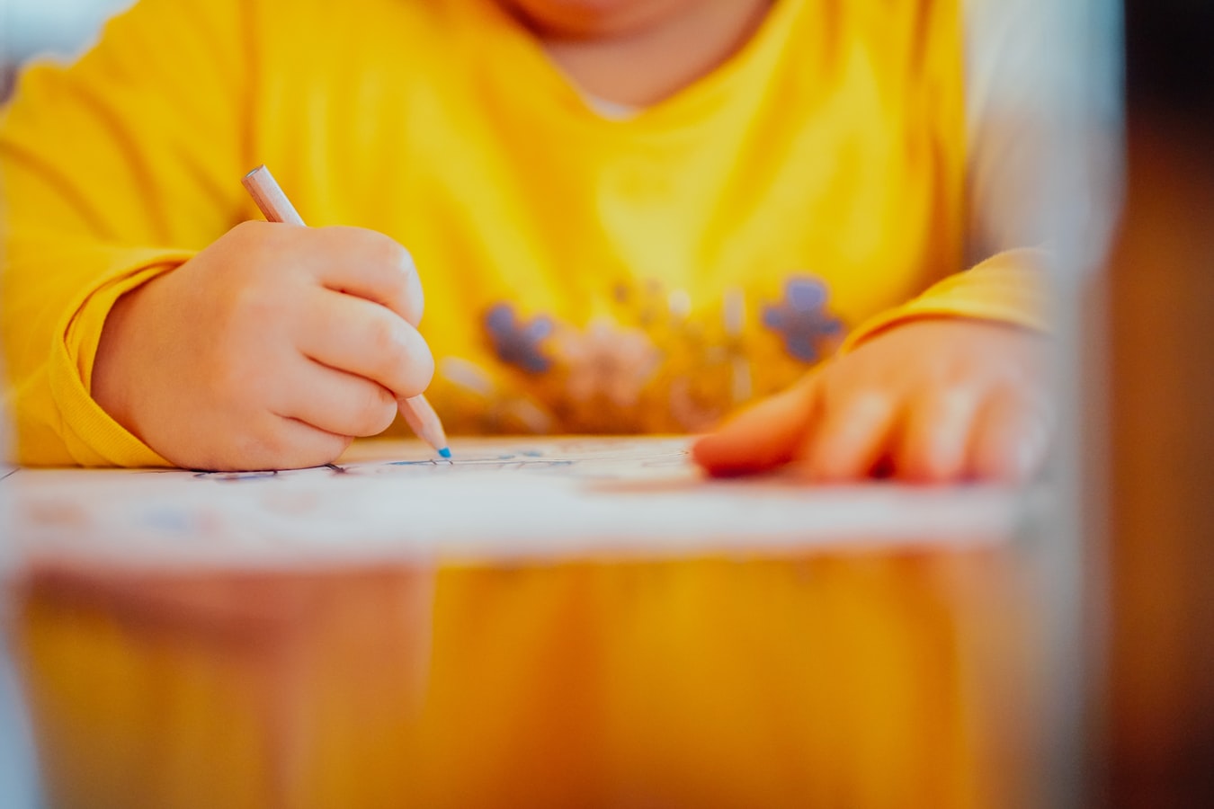 Kind im gelben Pullover malt mit einem Stift auf einem Blatt Papier