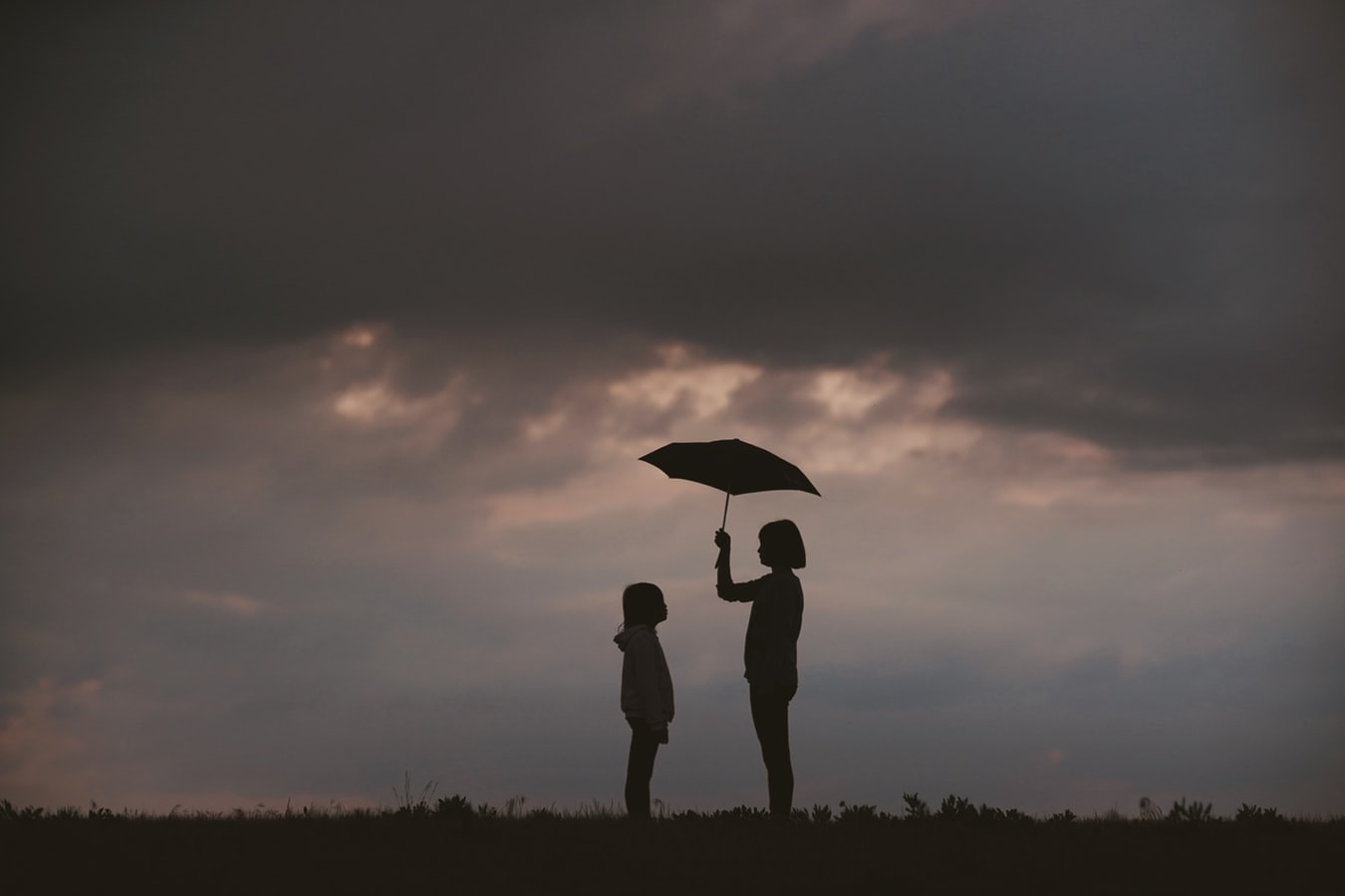 Silhouette einer Mutter, die einen Schirm über ihr Kind hält