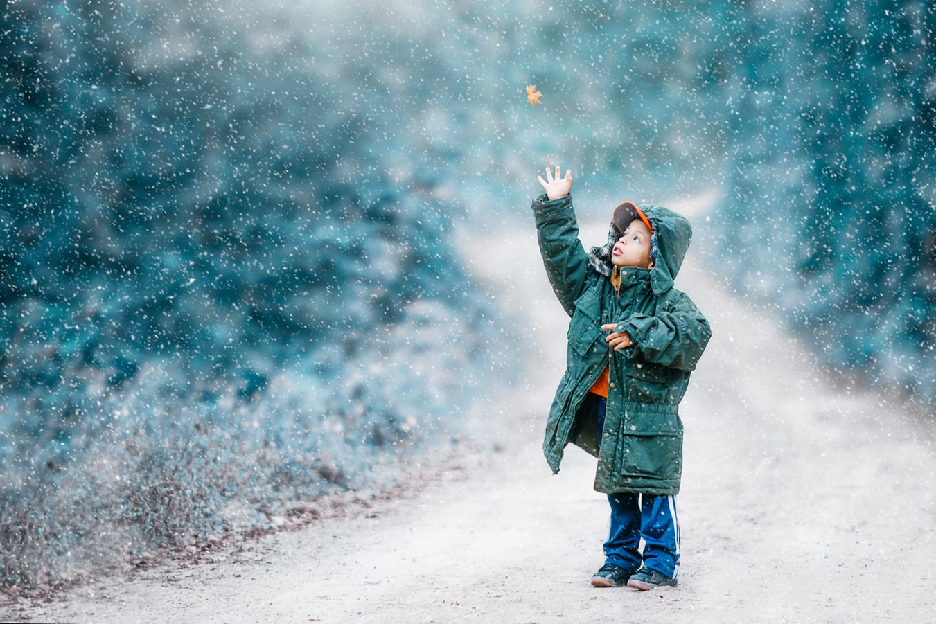 Kind in dicker Winterjacke streckt im Schneetreiben die Hand nach oben