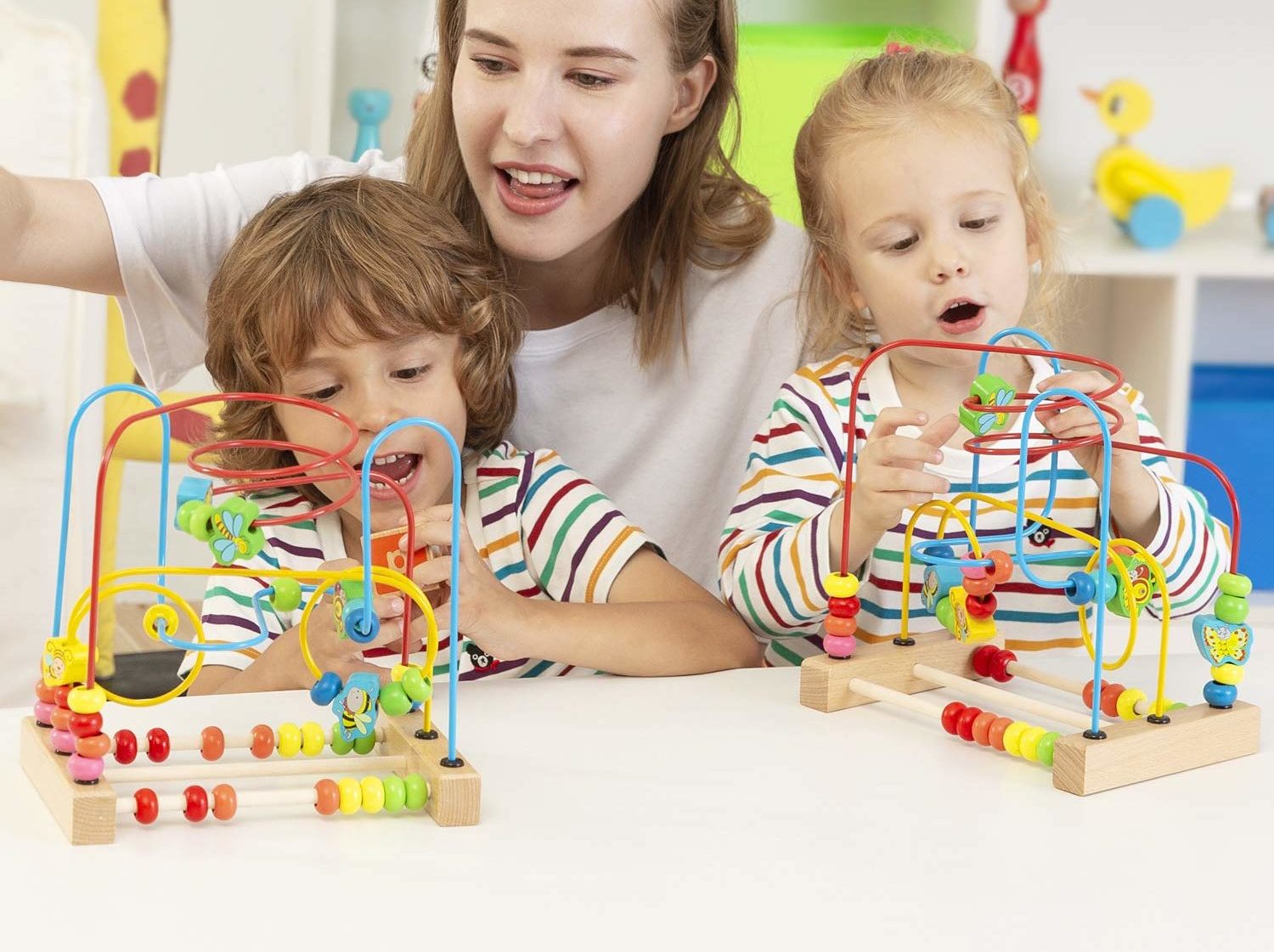 Erzieherin spielt mit zwei Kindern an bunten Motorikschleifen aus Holz