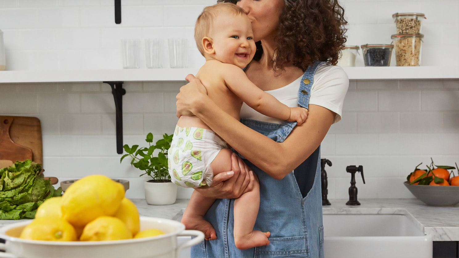Mutter küsst ihr Baby auf den Kopf, im Hintergrund eine Küche