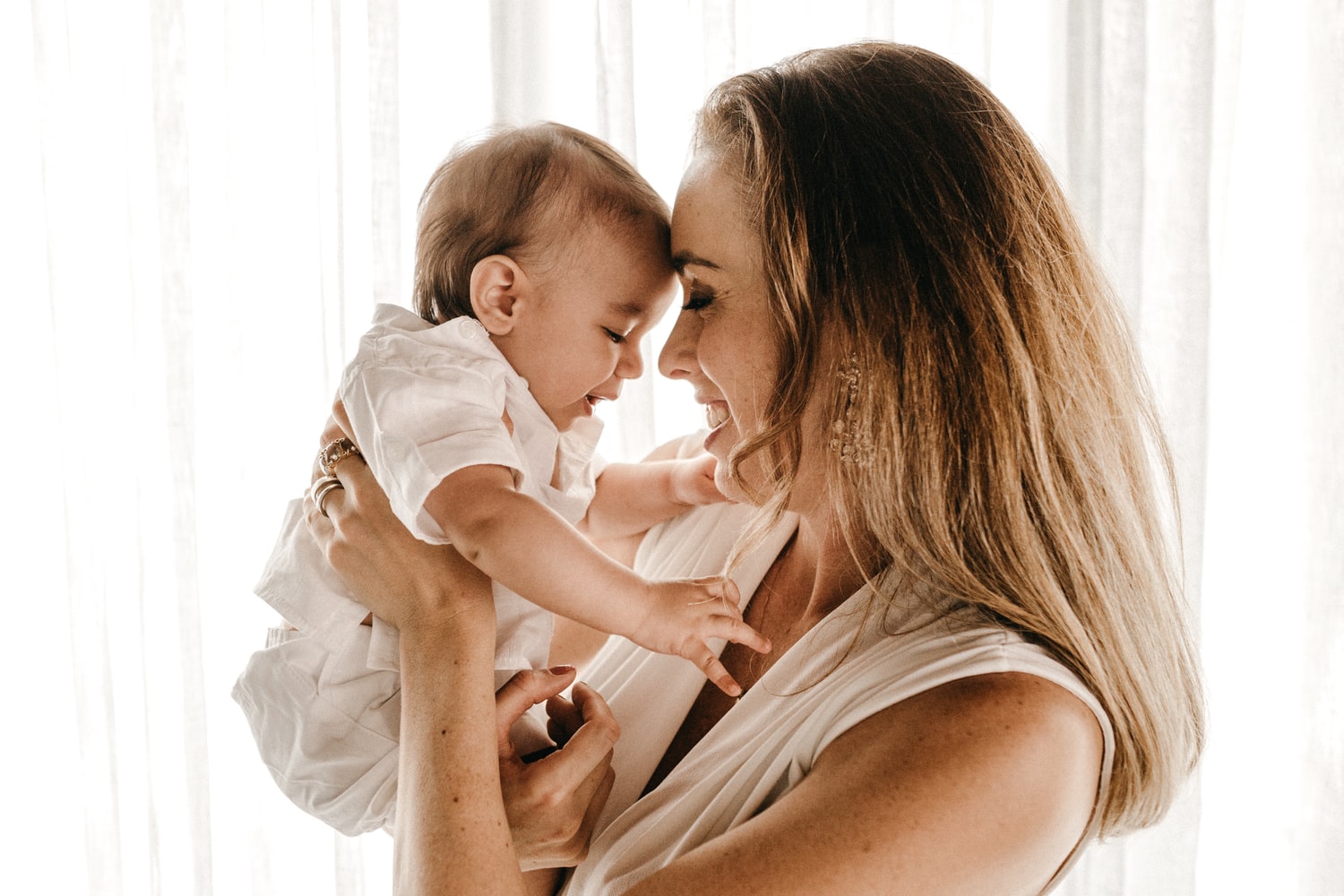 Mutter hält ihr Baby im Arm, Stirn an Stirn vor einem hellen Fenster