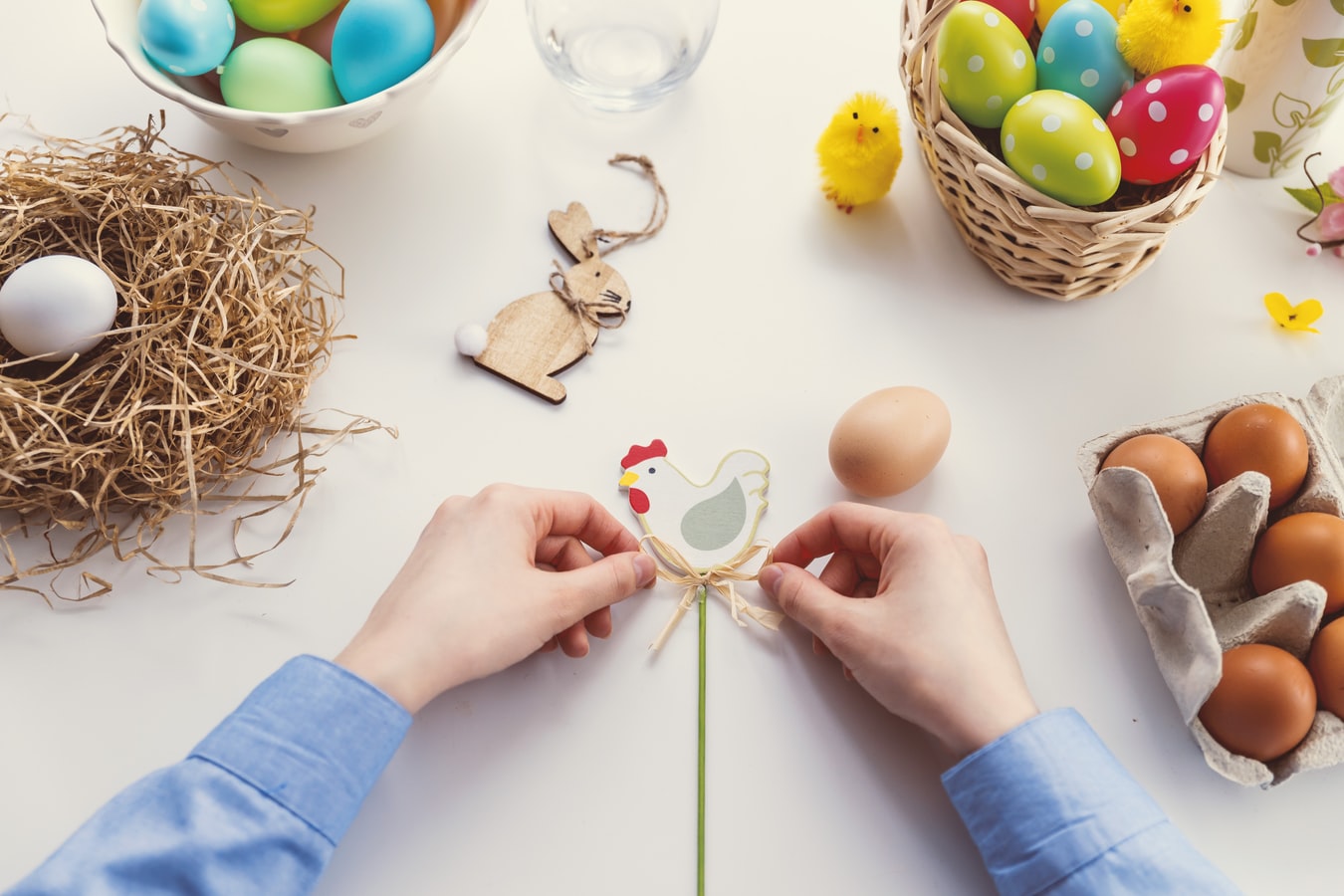 Hände basteln am Tisch mit Ostereiern, Nest und Küken eine Osterdekoration