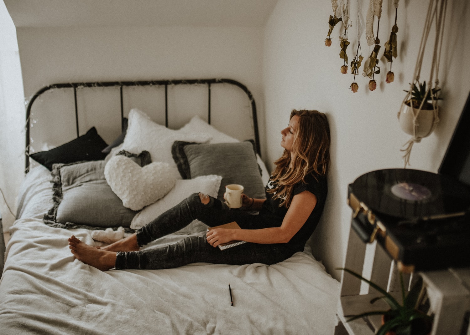 Frau sitzt mit einer Tasse Tee auf ihrem Bett