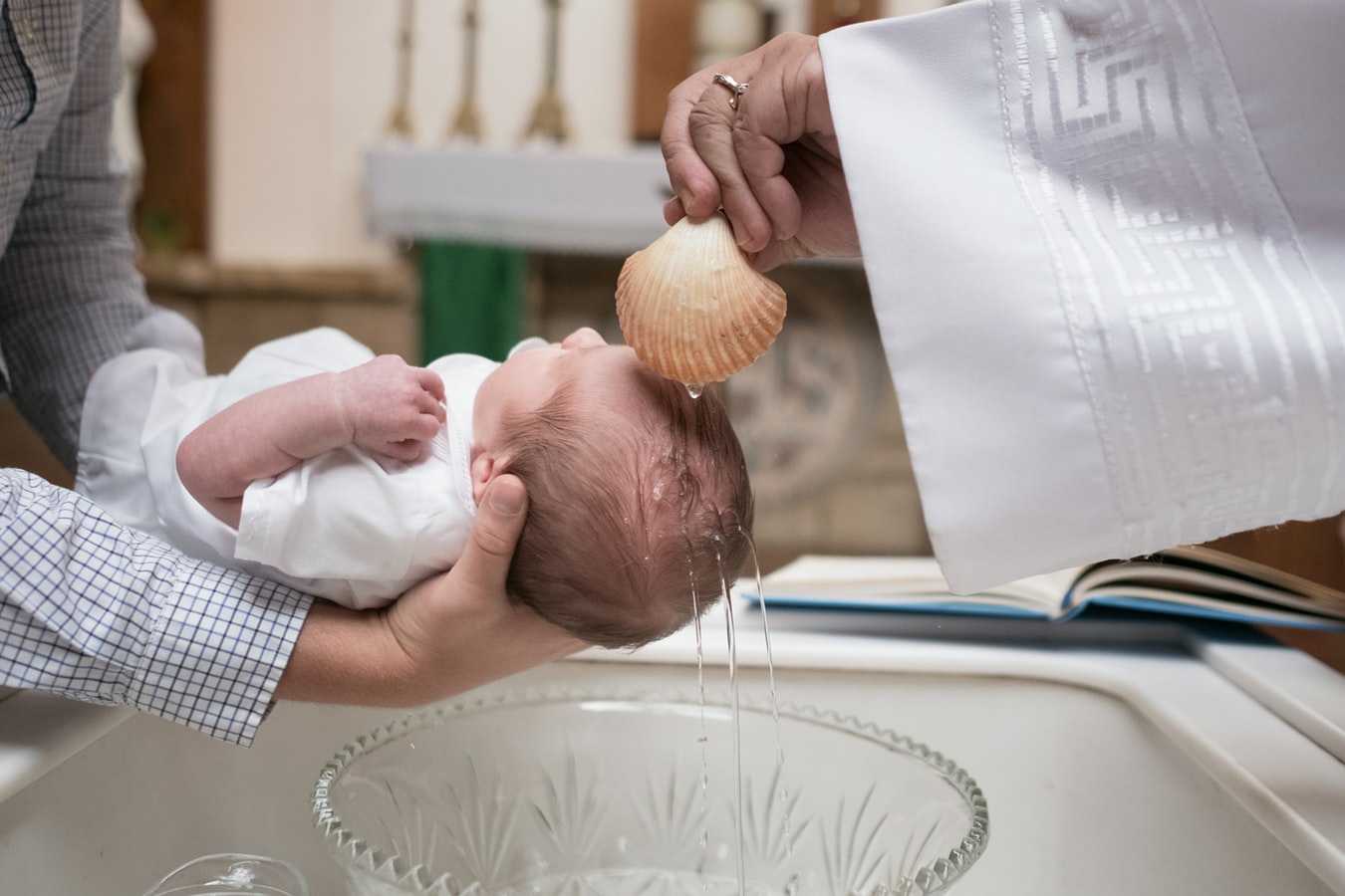 Bei der Taufe gießt der Pfarrer Wasser aus einer Muschel über den Kopf eines Babys